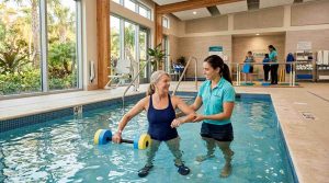 A modern Florida rehabilitation center with an indoor therapy pool, physical therapist assisting a middle-aged patient performing aquatic exercises.