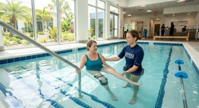 A modern rehabilitation center in Florida featuring a patient performing aquatic therapy with a licensed physical therapist inside a bright therapeutic pool